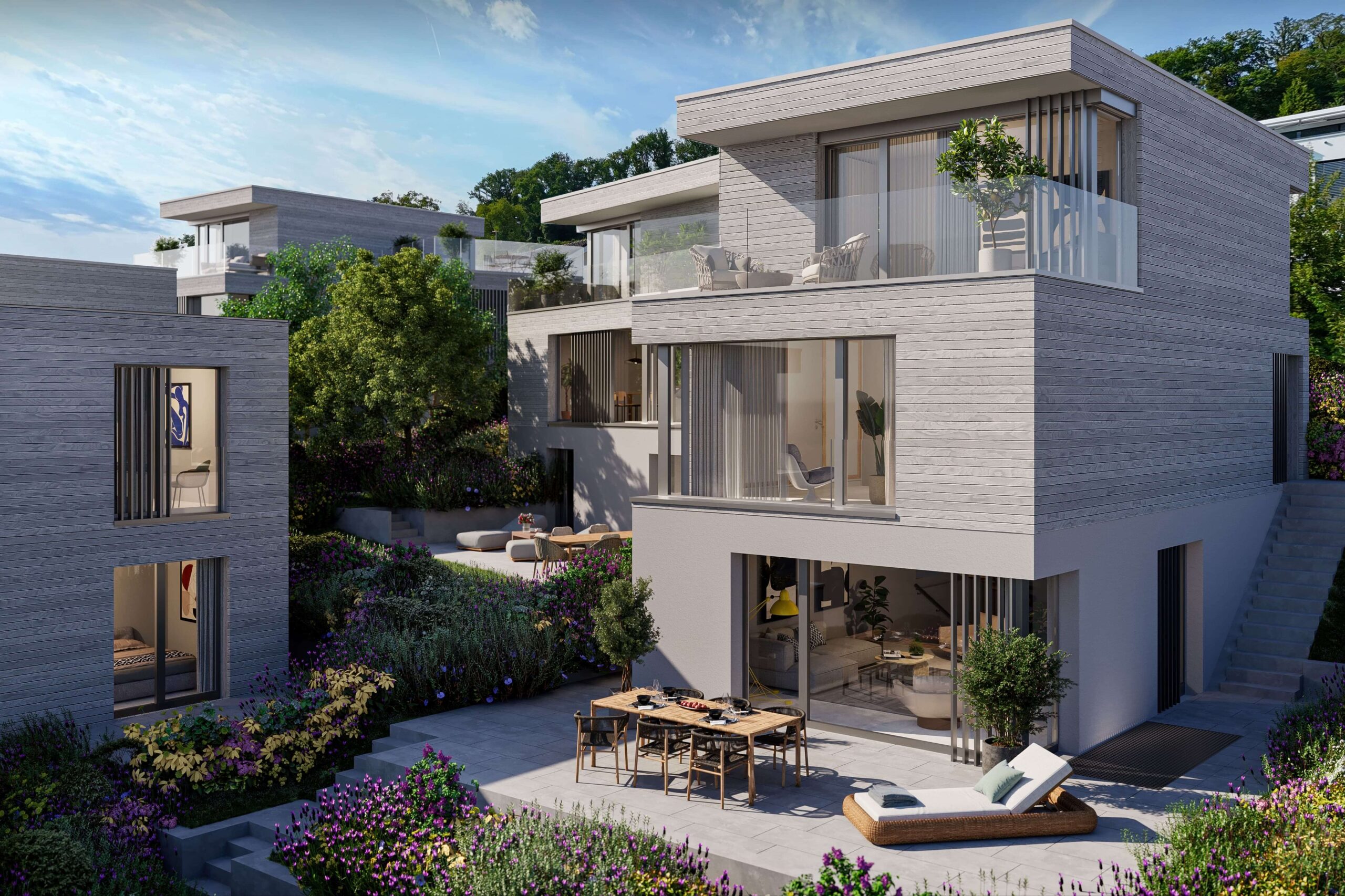 Moderne, terrassenförmig angeordnete Wohnhäuser des Projekts Biel-Benken Panorama der Ernst Frey AG, eingebettet in eine grüne, blühende Umgebung. Die Architektur besticht durch klare Linien, große Fensterflächen und großzügige Terrassen, die ein offenes, lichtdurchflutetes Wohnerlebnis mit Blick ins Grüne bieten.