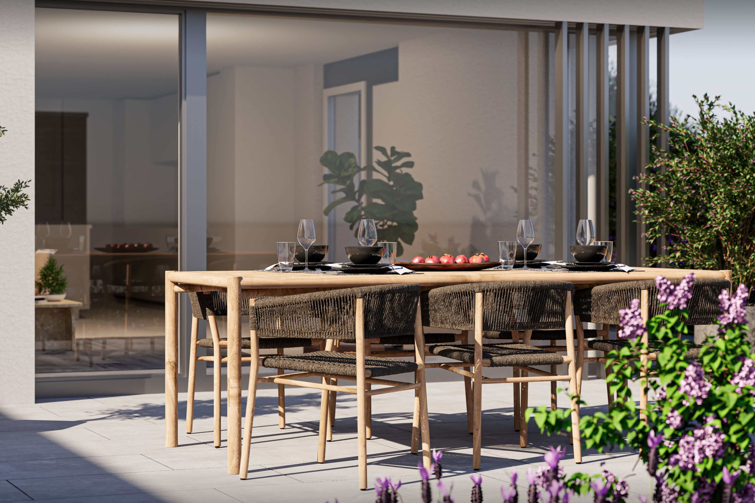 Ein stilvoll gedeckter Esstisch auf der Terrasse des Projekts Biel-Benken Panorama der Ernst Frey AG. Der Holztisch mit geflochtenen Stühlen steht inmitten blühender Pflanzen und lädt zum Essen im Freien ein. Durch die großen Glasfronten entsteht ein fließender Übergang zwischen Innen- und Außenraum.